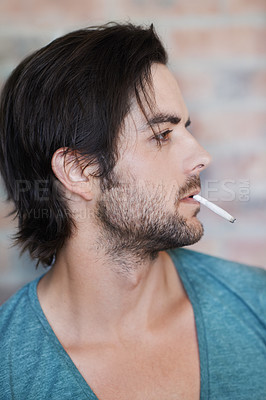 Buy stock photo Man, cigarette and urban fashion by brick wall in city for style, edgy and thinking outdoors. Smoking, male person and streetwear by building for addiction, stress relief and relaxation outside