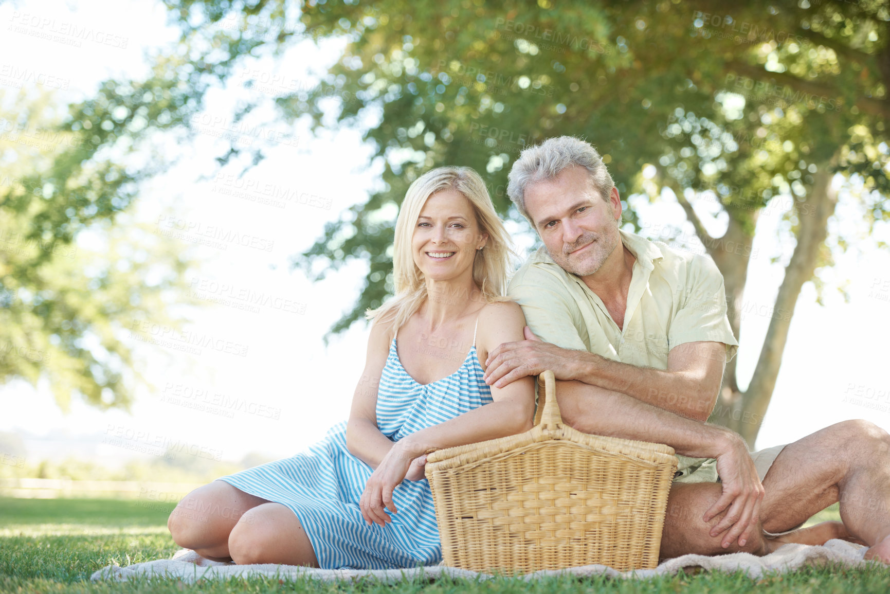 Buy stock photo A happy husband and wife sitting in a park with a picnic basket