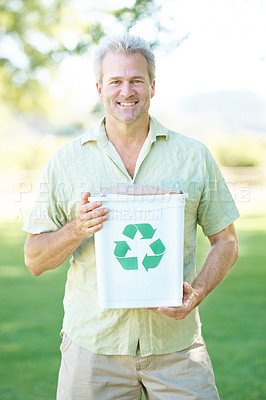 Buy stock photo A man standing in a park holding a recycling bin while smiling at the camera
