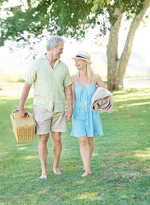 Buy stock photo A happy couple walking in the park looking for a spot to set up their picnic
