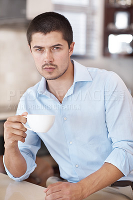 Buy stock photo A handsome male sitting in his kitchen holding a cup of coffee