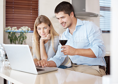 Buy stock photo A happy couple enjoying a glass of wine in their kitchen looking on a laptop together