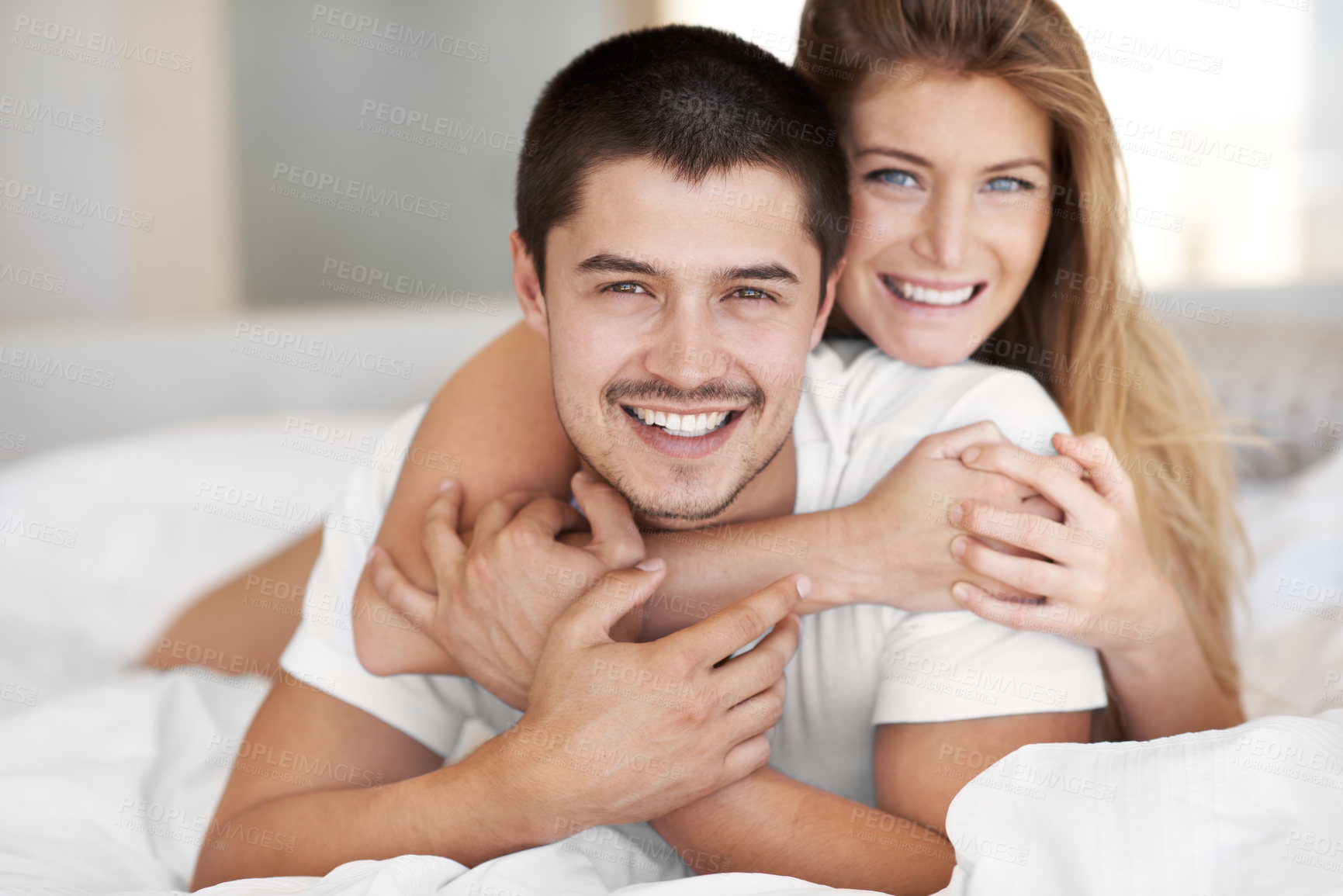 Buy stock photo Attractive young woman embracing her partner while they lie in bed together