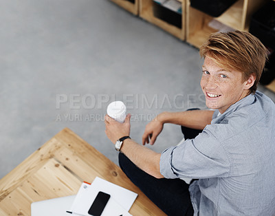 Buy stock photo High angle portrait of a young employee holding a cup of coffee while sitting in the office. A handsome male student taking a study break after lectures. One designer relaxing in a creative workplace