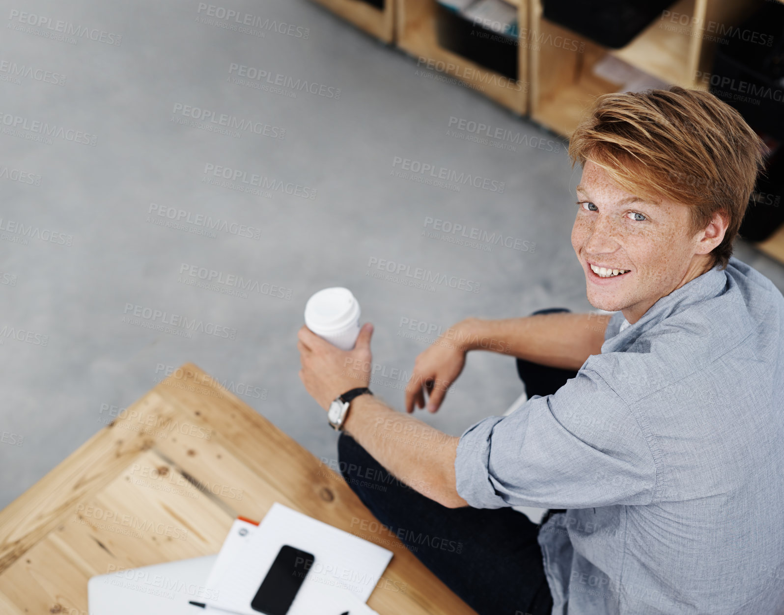 Buy stock photo High angle portrait of a young employee holding a cup of coffee while sitting in the office. A handsome male student taking a study break after lectures. One designer relaxing in a creative workplace