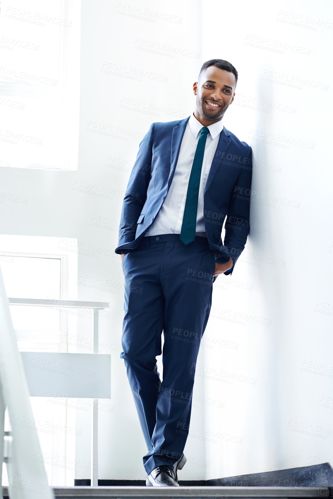 Buy stock photo A handsome african american businessman leaning against a wall indoors