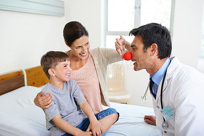 Buy stock photo Shot of a doctor attempting to distract his young patient with a clown's nose