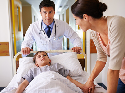 Buy stock photo Shot of a concerned mother watching her son being wheeled down the hospital passage