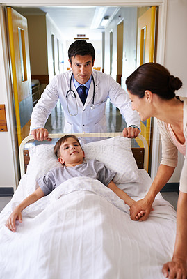 Buy stock photo Shot of a doctor wheeling a young patient down a corridor