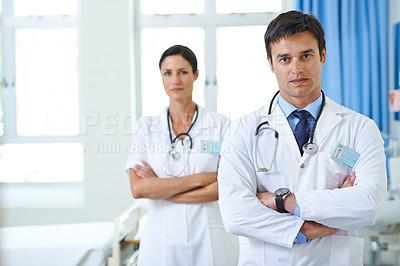 Buy stock photo Portrait of a handsome young doctor with his nursing assistant in the background