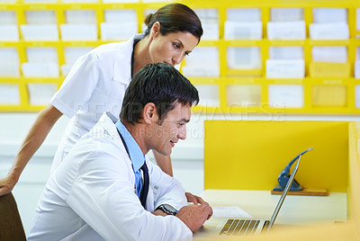 Buy stock photo Shot of a handsome young doctor and his nursing assistant looking at a laptop screen