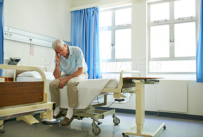 Buy stock photo Shot of a senior man in pain sitting alone on a bed in a hospital ward