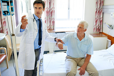 Buy stock photo Shot of a handsome young doctor attending to a senior man in a hospital ward