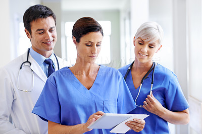 Buy stock photo Shot of three young doctors going through a patient's file on a tablet