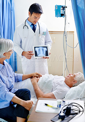 Buy stock photo Shot of a sick man in a hospital bed being shown an xray of his chest while his wife holds his hand