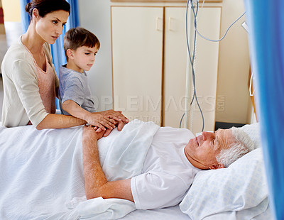 Buy stock photo Shot of a sick man in a hospital bed being comforted by his daughter and grandson