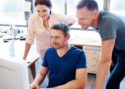 Buy stock photo Shot of three coworkers looking at a computer screen in an office