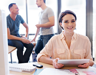 Buy stock photo Portrait of an office worker using a tablet while her coworkers have a discussion in the background