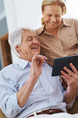 Buy stock photo Shot of a senior man sharing a joke on his digital tablet with his wife