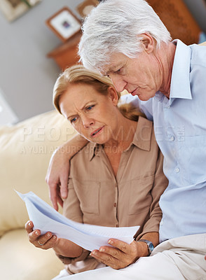 Buy stock photo Shot of a senior couple looking seriosly at documents