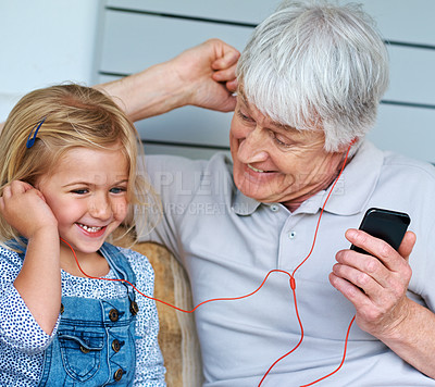 Buy stock photo Shot of an adorable little girl listening to music from a cellphone with her grandfather