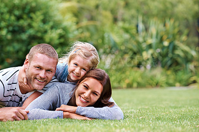 Buy stock photo Portrait of a happy family of three lying outside on the grass