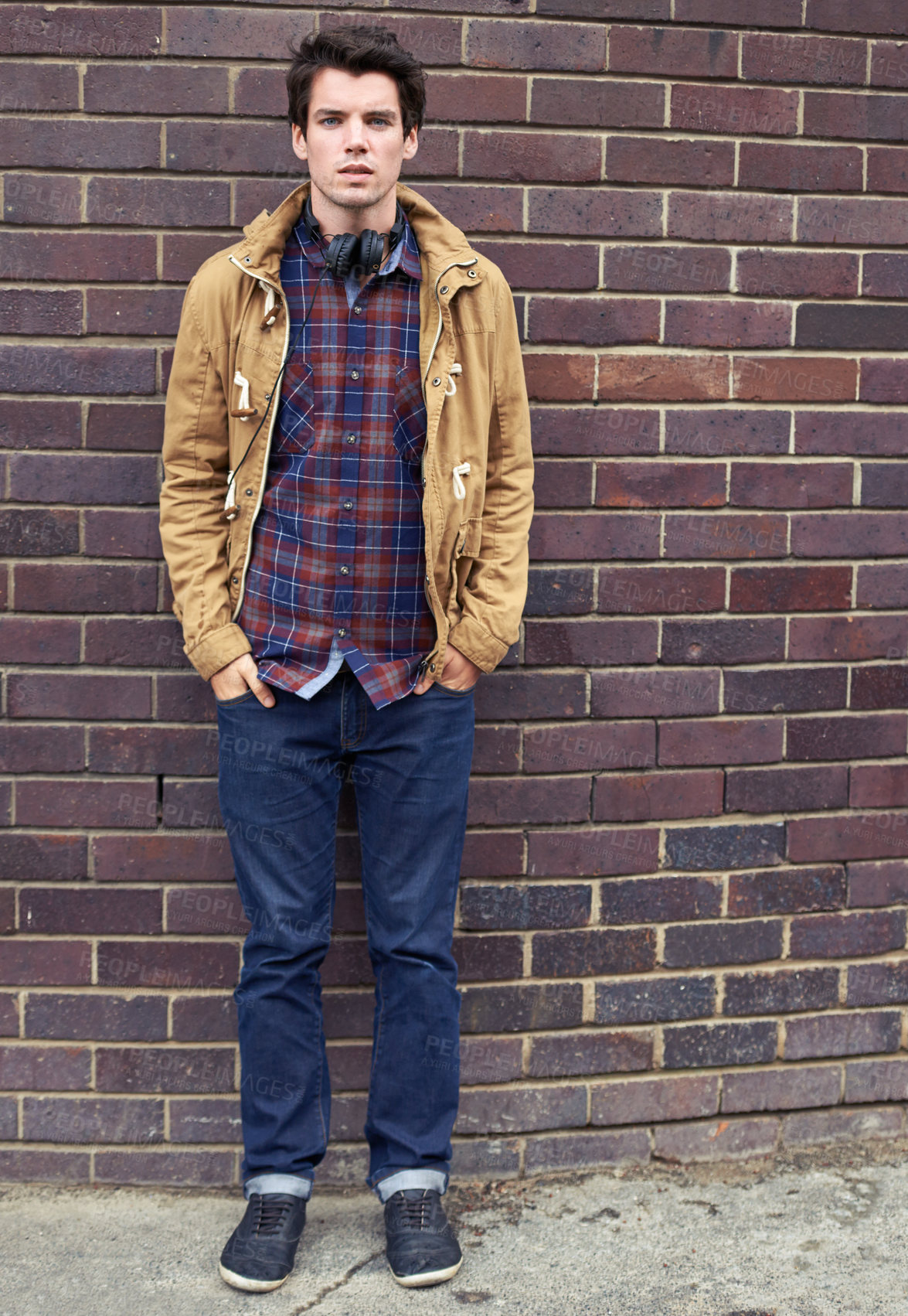 Buy stock photo Man, street fashion and portrait at brick wall with confidence, headphones or relax on sidewalk. Student, casual and hands in pockets in city for attitude, style or edgy in urban New York for commute