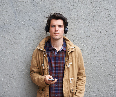 Buy stock photo Man, fashion and portrait at wall with headphones, phone and relax on sidewalk. Student, streetwear and mobile with music for streaming app, podcast and favorite playlist on commute in New York