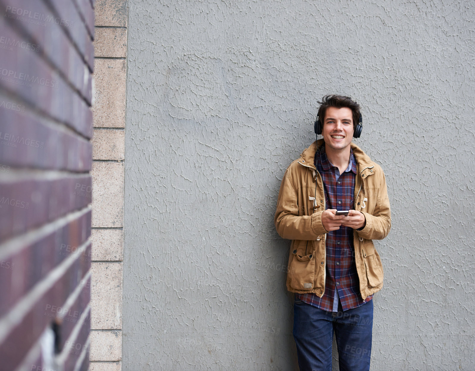 Buy stock photo Portrait, headphones or happy man with phone by wall for communication, connection or chat. Mobile, texting or student in city on urban street for music app, social media website or news notification