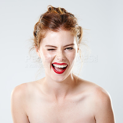 Buy stock photo Beauty portrait of a playful woman wearing red lipstick and makeup against grey studio background. Headshot of flirty redhead model posing shirtless and winking. Facial expression of silly goofy woman