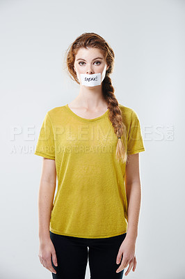 Buy stock photo Cropped studio portrait of a young woman with a label saying 'speak!' covering her mouth