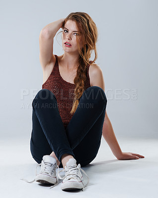 Buy stock photo Portrait of a beautiful young woman in casualwear sitting with her legs crossed on the studio floor
