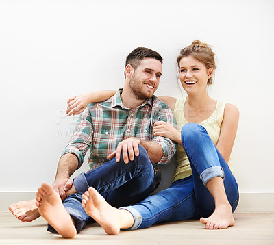 Buy stock photo Shot of an affectionate young couple sitting beside each other on the floor at home