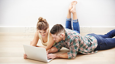 Buy stock photo Shot of a loving young couple using a laptop while lying on the floor at home