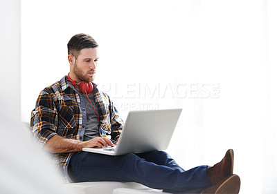 Buy stock photo Handsome young man using a laptop while relaxing on the couch at home. Content male browsing online using social media on a computer in the living room. Man working from home on his laptop