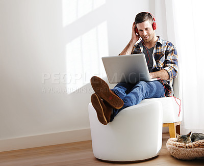 Buy stock photo Shot of a young man listening to music at home on his laptop