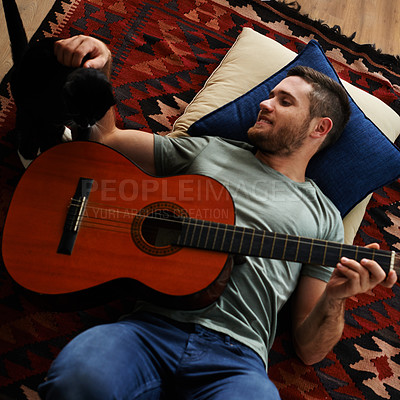 Buy stock photo Shot of a young man with a guitar lying on the floor with his cat