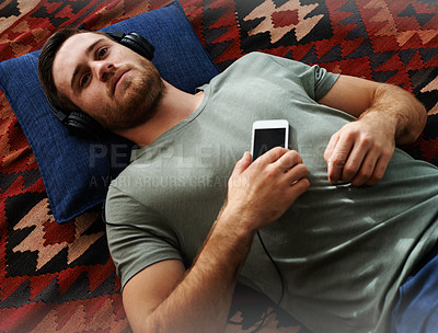 Buy stock photo Shot of a young man lying on the floor listening to music 