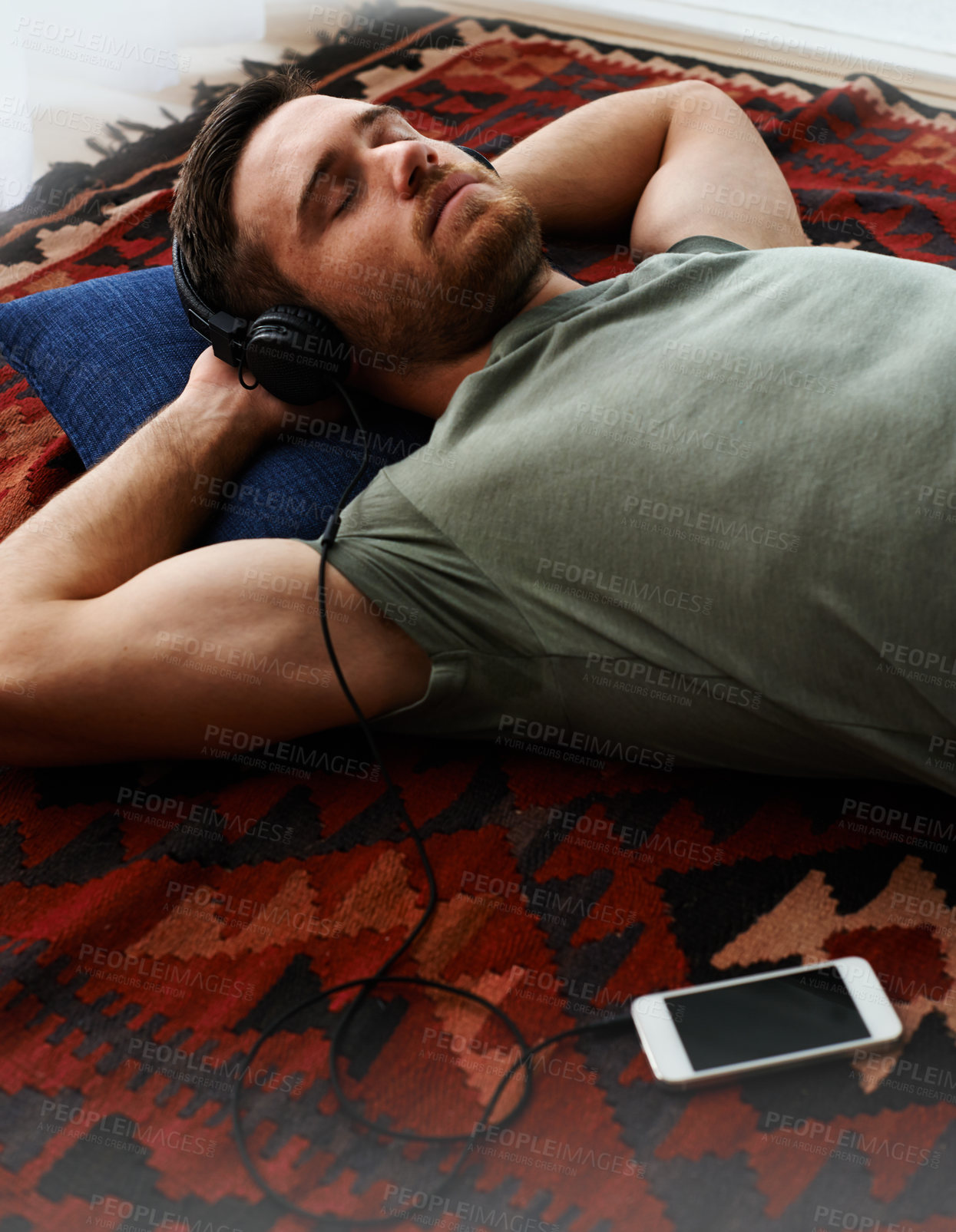Buy stock photo Shot of a young man lying on the floor listening to music 