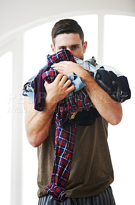 Buy stock photo Portrait of a young white man holding an heap of laundry. A good looking man at home holding bunch of cloths. Portrait of young man carrying dirty clothes for the washing. Man holding pile of shirts