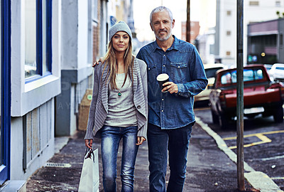 Buy stock photo A beautiful young woman and her father walking with a shopping bag and takeaway coffee in the city
