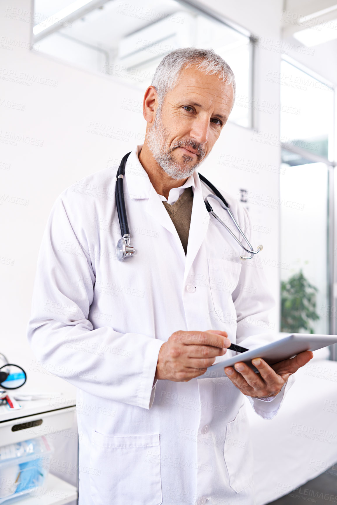 Buy stock photo Portrait of a mature male doctor standing with a digital tablet in a medical building