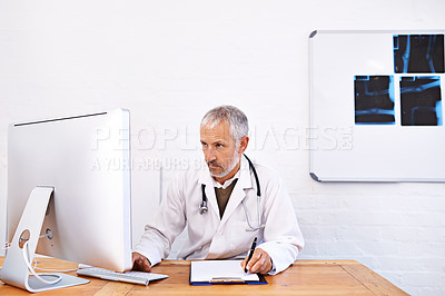 Buy stock photo Shot of a mature male doctor working at a desktop computer in his office