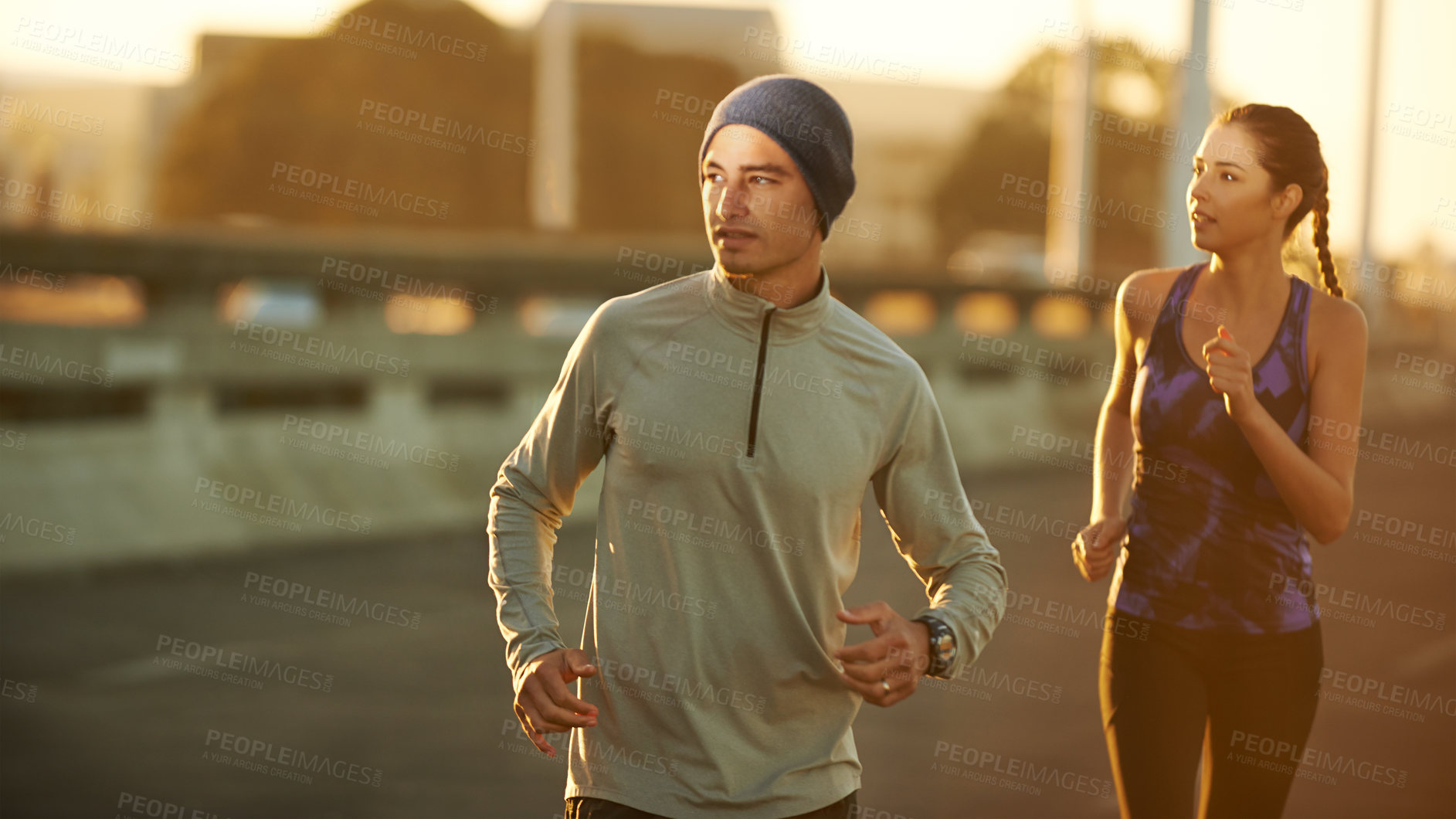 Buy stock photo Shot of two friends jogging down a road in the early morning