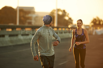 Buy stock photo Shot of two friends jogging down a road in the early morning