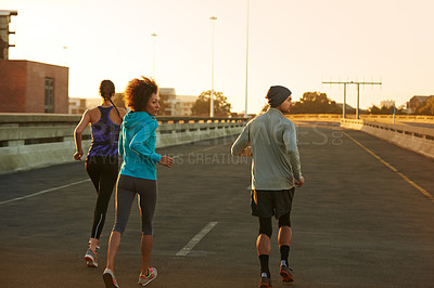 Buy stock photo Rearview shot of three young joggers running down an empty street at dawn