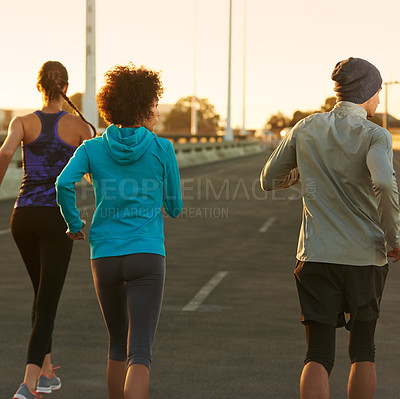 Buy stock photo Urban, road and people running at sunset together for fitness, training or commitment to body health. Evening, exercise and group of friends on street in city workout with outdoor challenge from back