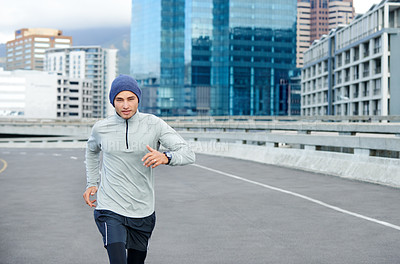 Buy stock photo Shot of a young man jogging through empty city streets