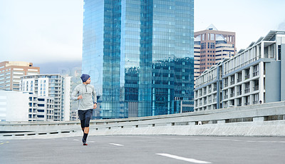 Buy stock photo Shot of a young man jogging through empty city streets
