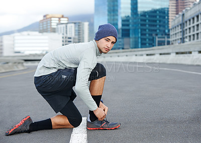 Buy stock photo Portrait of a young man tying up his shoelaces before a run through the city